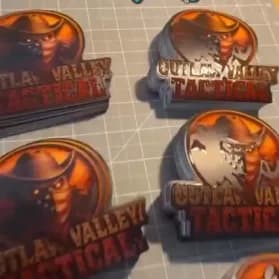 3D printed Outlaw Valley Tactical logo badges laid out on a printer bed.
