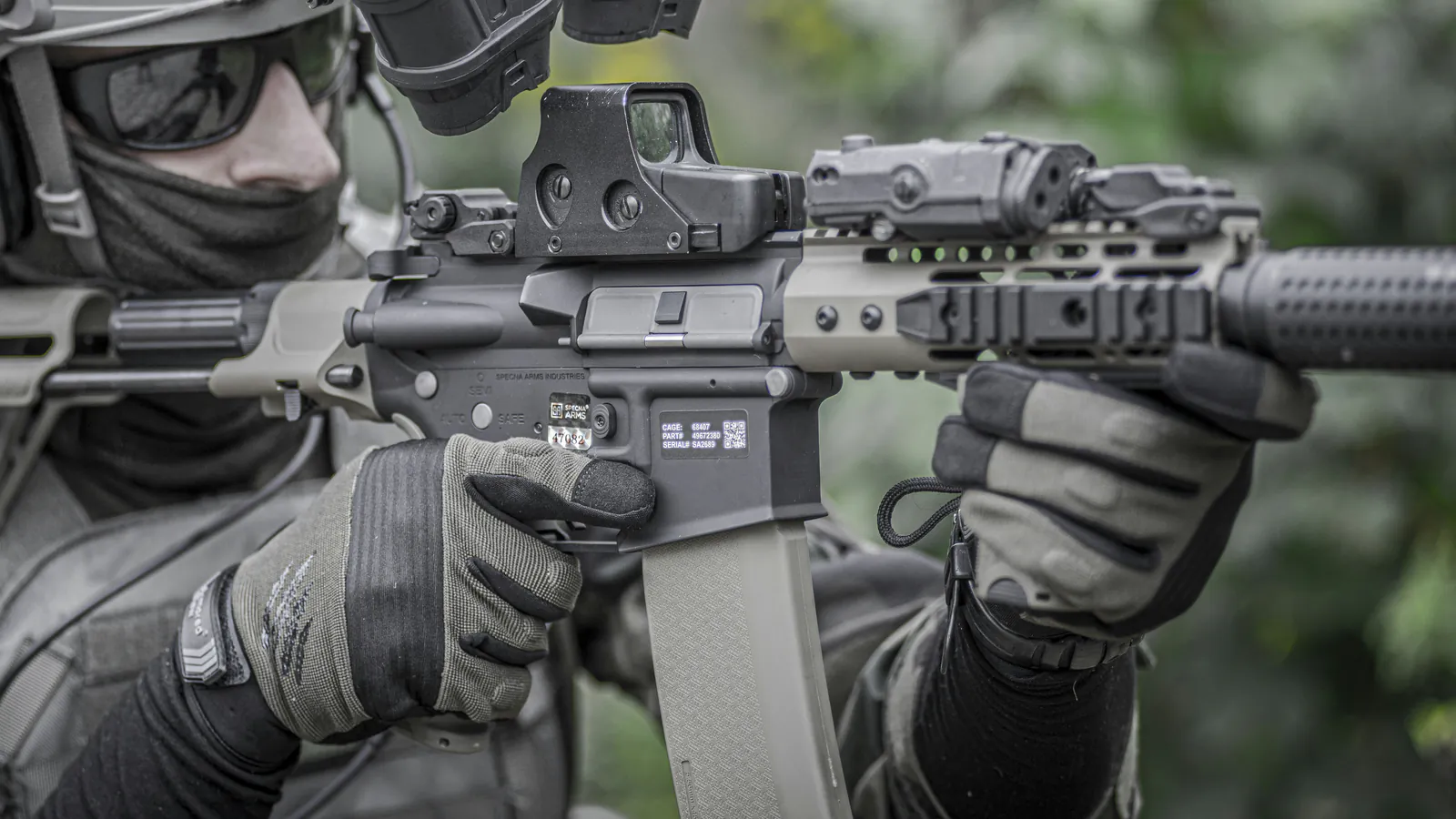 A shooter presses his cheek to the stock behind a carbine whose holographic sight stands clear of the receiver rail on a tall mount, with a laser unit set further forward on the handguard